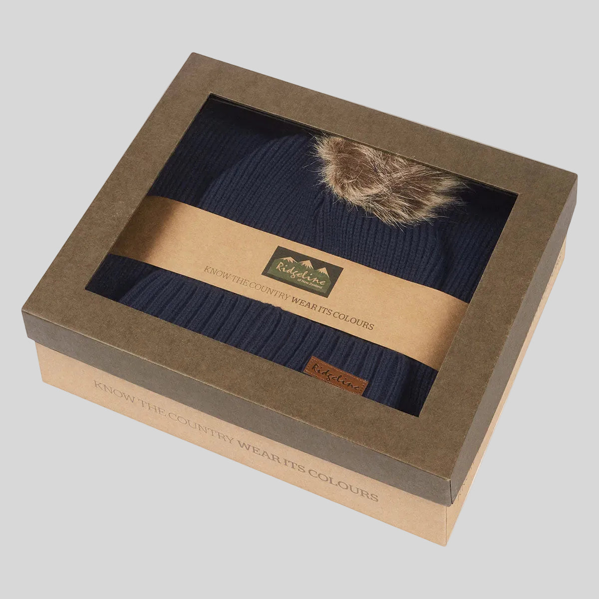 Navy ribbed knit beanie hat with faux fur pom pom in windowed gift box, angled view.
