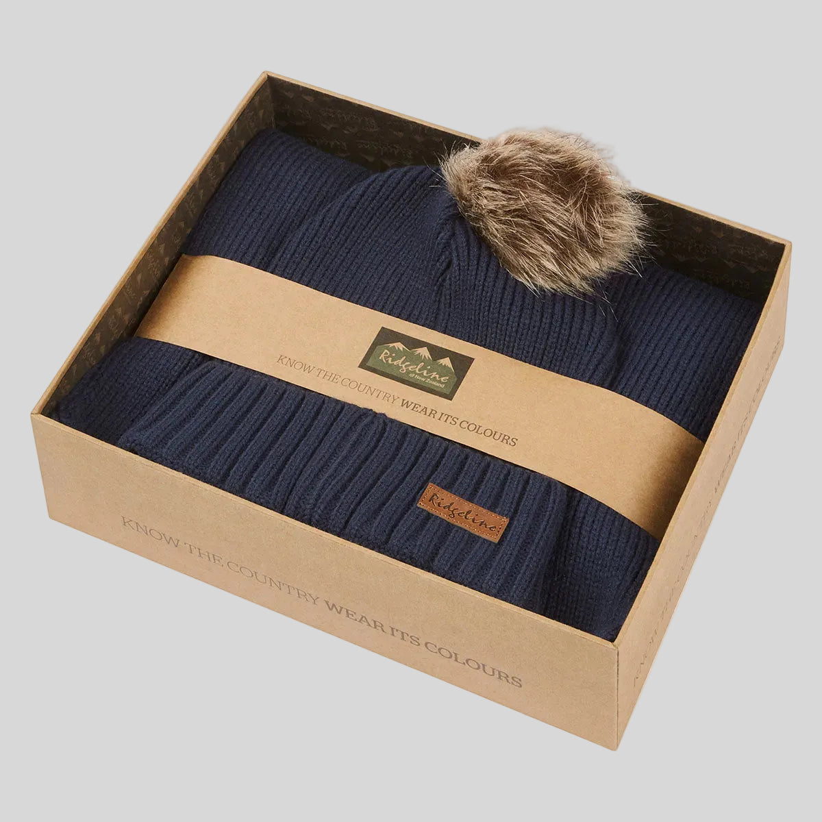 Navy ribbed knit beanie hat with faux fur pom pom in branded gift box, angled view.