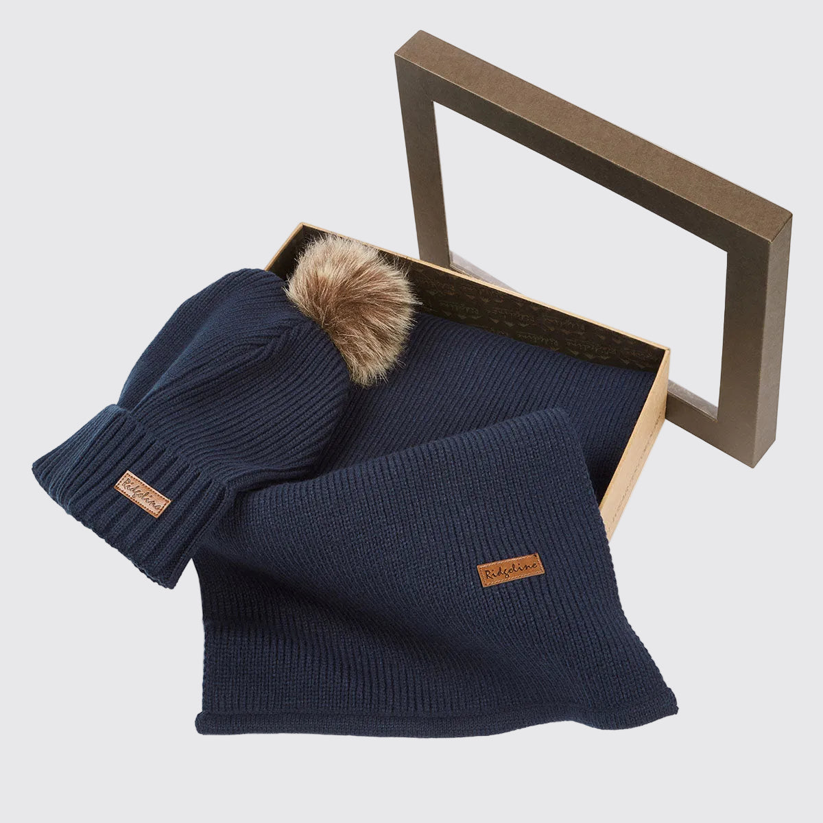 Navy ribbed knit beanie hat with faux fur pom pom and matching scarf in open gift box, angled view.