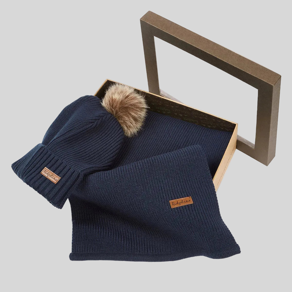 Navy ribbed knit beanie hat with faux fur pom pom and matching scarf in open gift box, angled view.