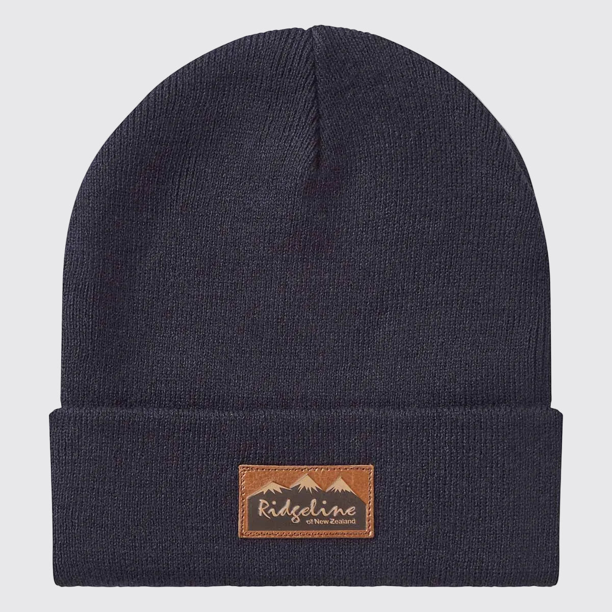 Front view of a navy blue ribbed knit beanie with a folded cuff, displayed against a light grey background. A brown faux-leather patch is centered on the cuff, featuring a mountain graphic and the text “Ridgeline of New Zealand.” The simple, classic design and stretch-knit construction are clearly visible, highlighting the beanie's snug fit and everyday outdoor style.