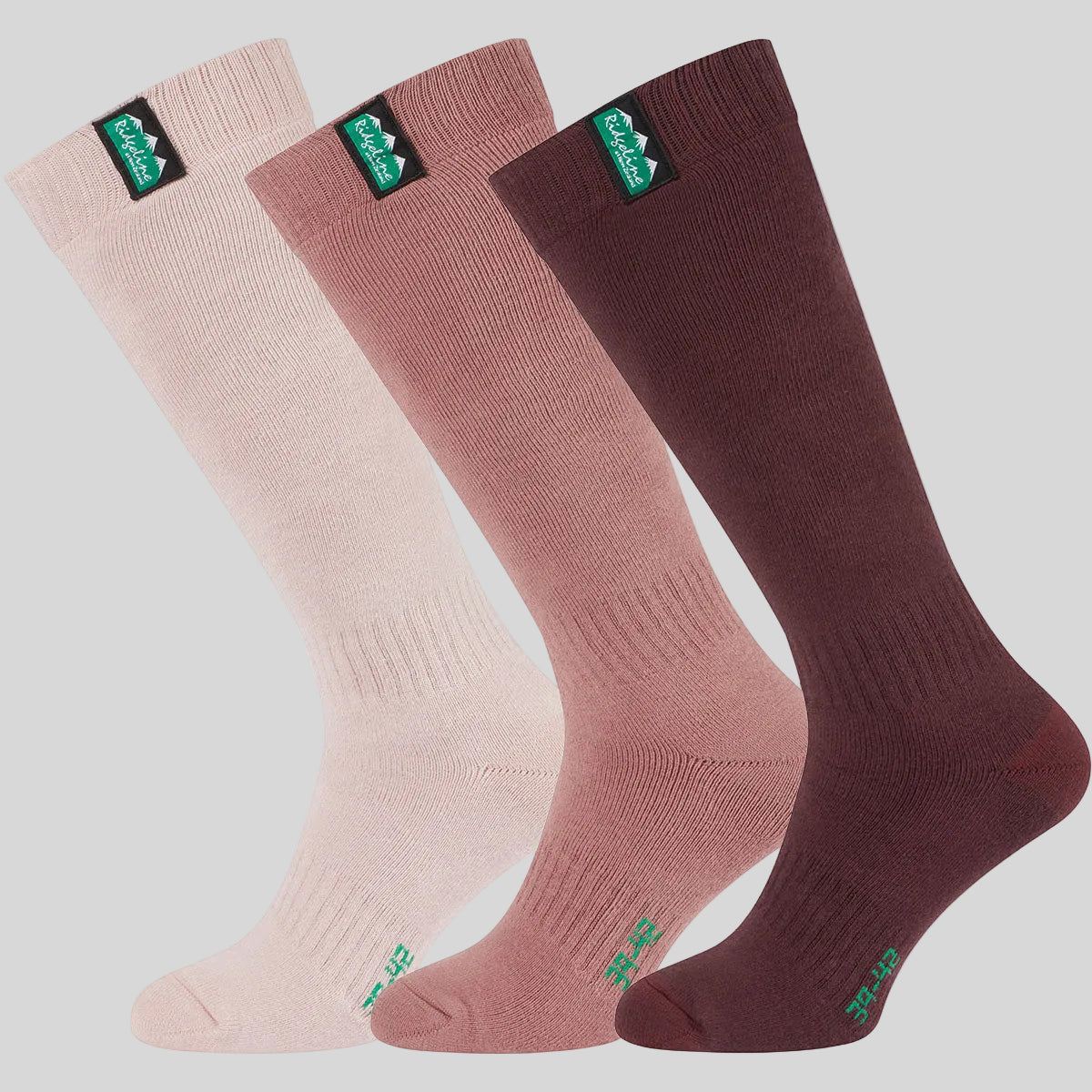 Three knee-high socks in light pink, dusty rose, and dark burgundy, arranged diagonally on a grey background. Each sock has a green and black 'Ridgeline' logo patch near the cuff.