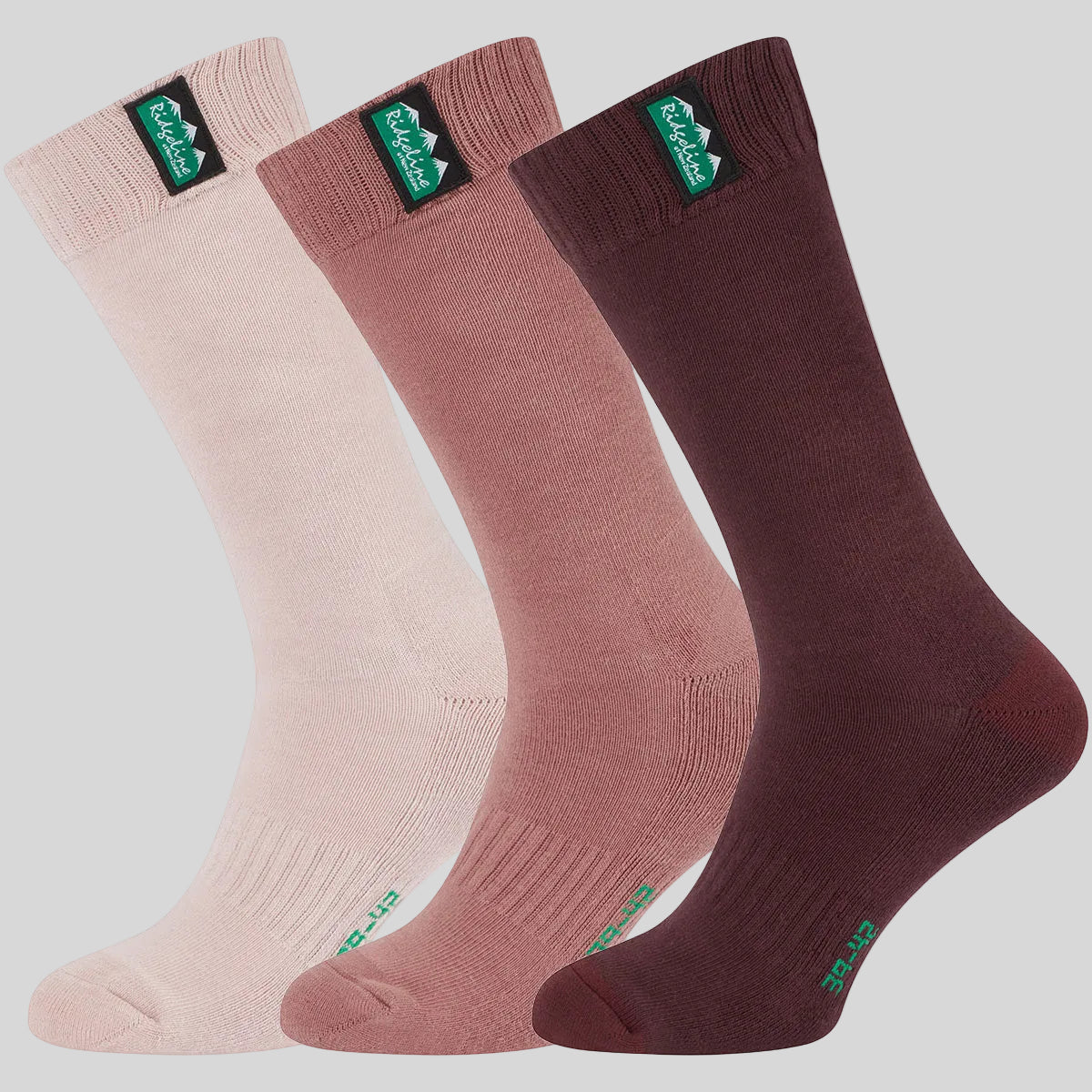 Three pairs of crew socks in light pink, dusty rose, and dark burgundy, arranged diagonally on a grey background. Each sock features a green and black CampMaid logo patch on the cuff and the brand name 'Ridgeline' printed near the top.