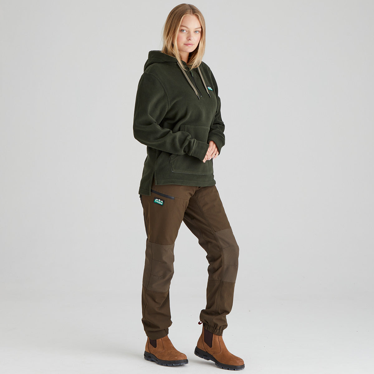 Person wearing a green Fleece hoodie and brown pants on a light grey background