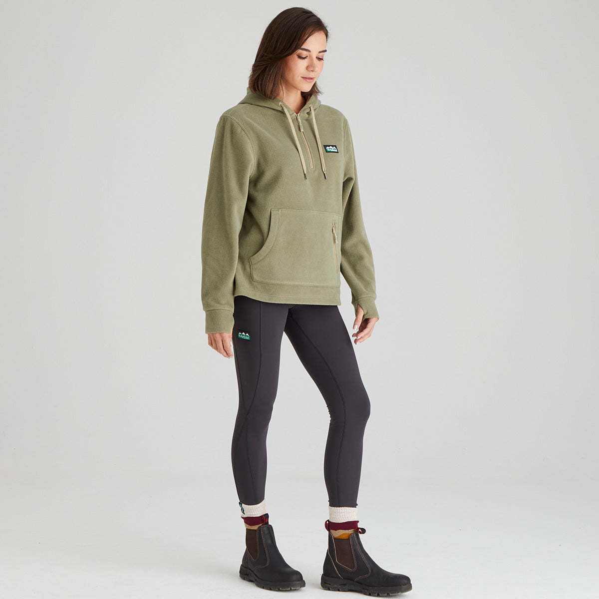 Person wearing a green fleece hoodie and dark leggings on a light grey background