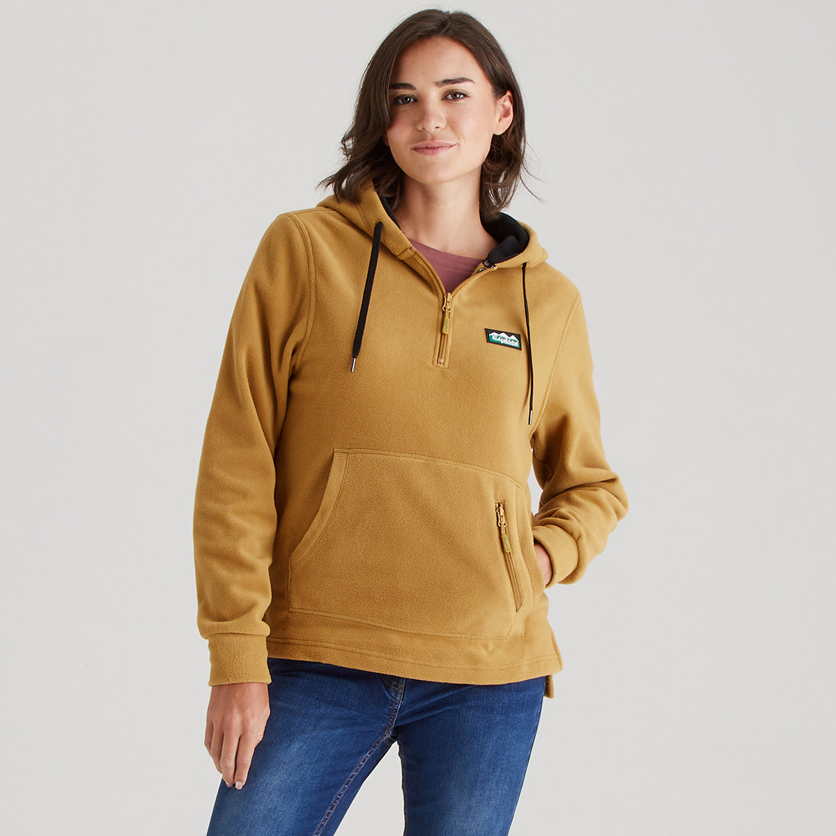 Woman wearing a mustard yellow hoodie with a brand logo on a light gray background