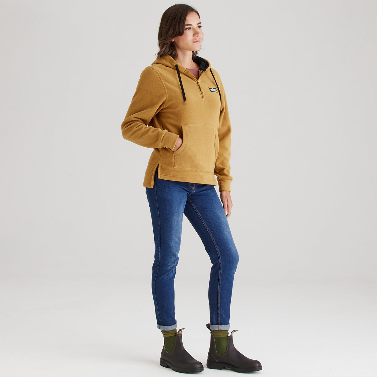 Woman wearing a mustard yellow jacket, blue jeans, and black boots on a white background