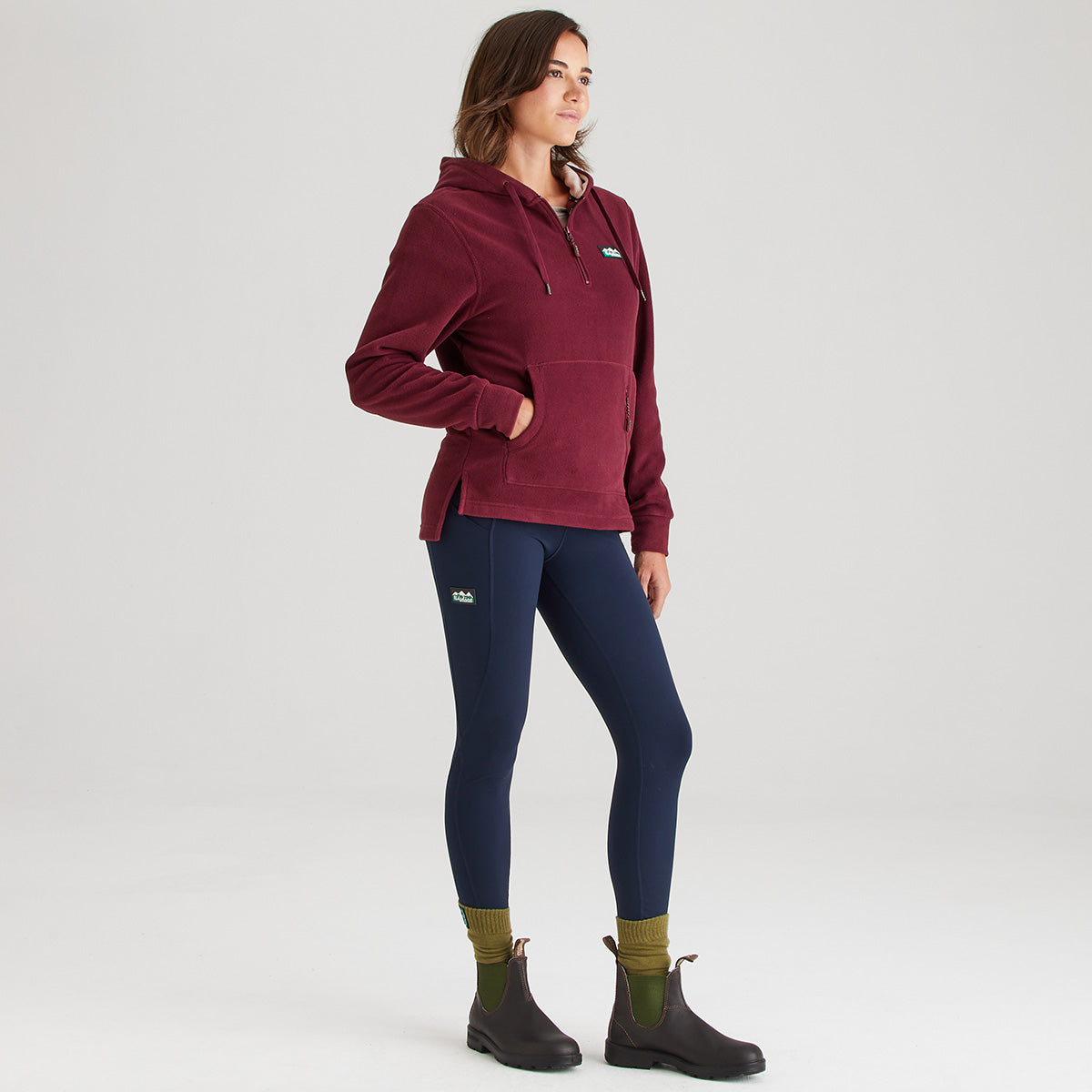 Woman wearing a maroon pullover and navy leggings on a white background
