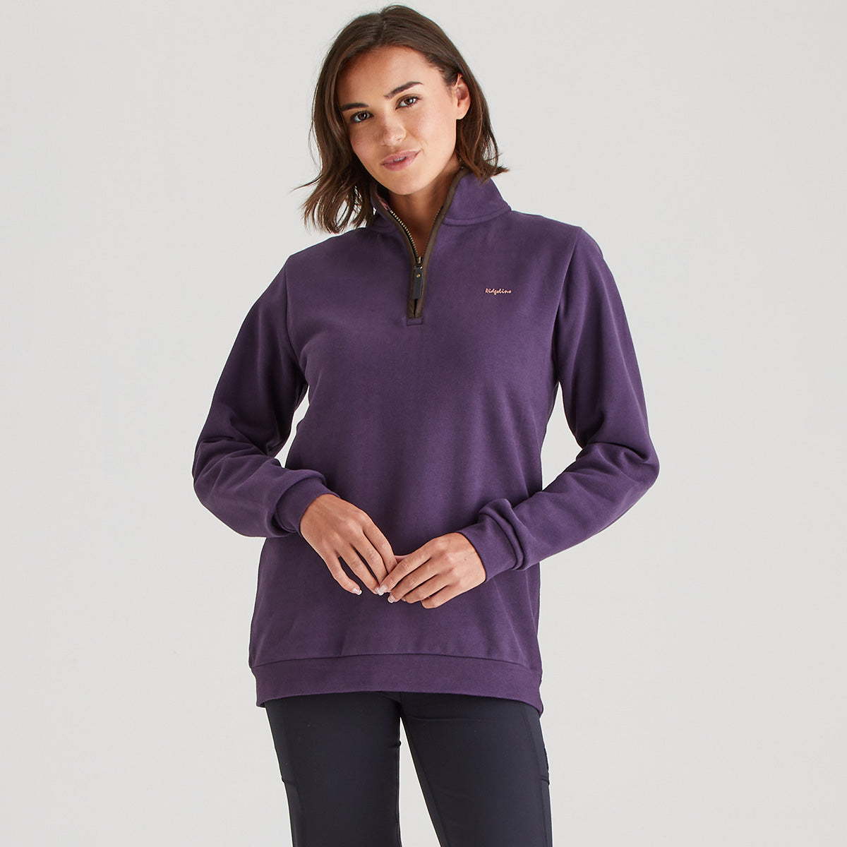 Woman wearing a purple pullover with a brand logo on a light gray background