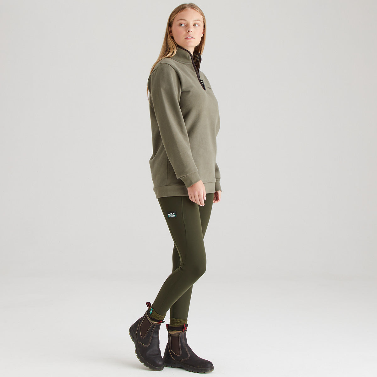 Person wearing a green pullover and pants with black boots on a white background