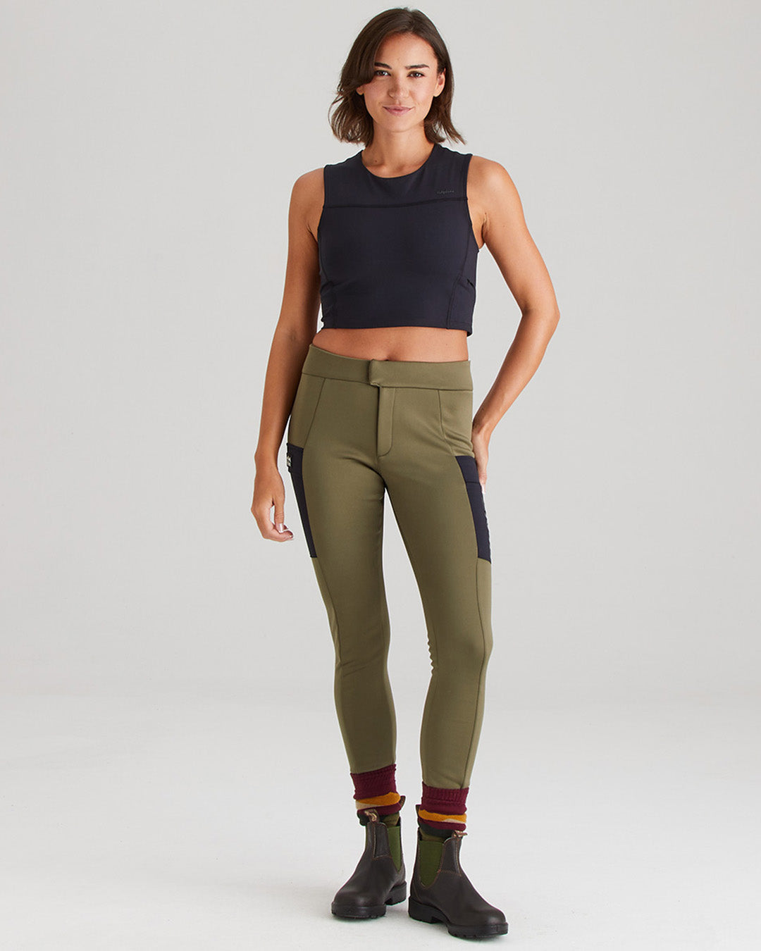 Woman wearing olive green riding pants with black accents on a white background