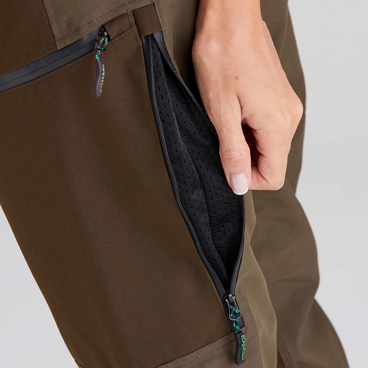 Brown pants with a hand opening a zipper pocket on a light gray background