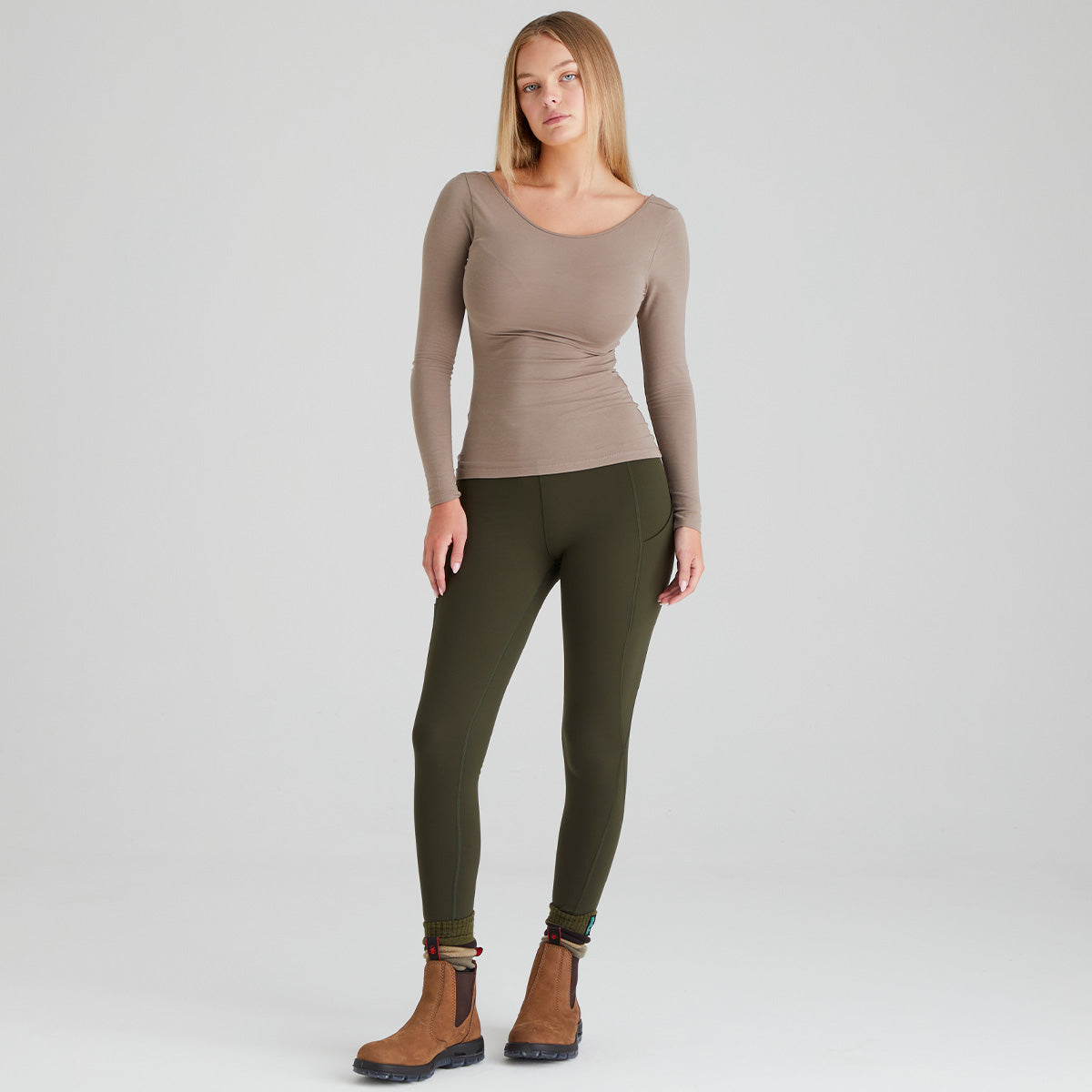 Woman wearing a brown long-sleeve top and green leggings on a white background