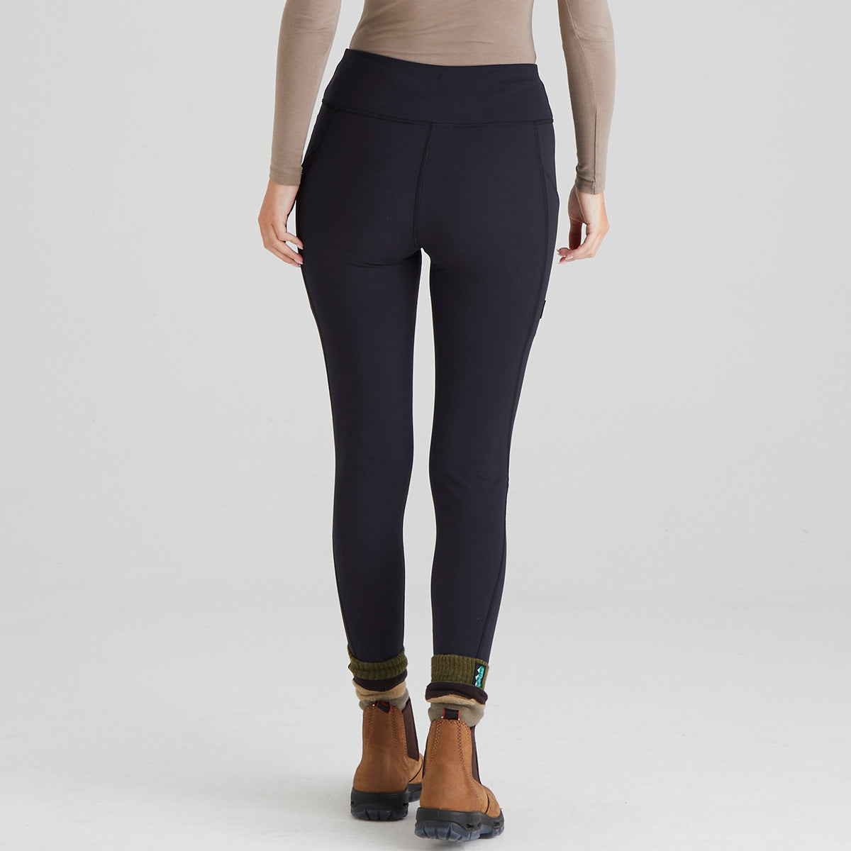 back view of person wearing black leggings with brown boots on a light grey background