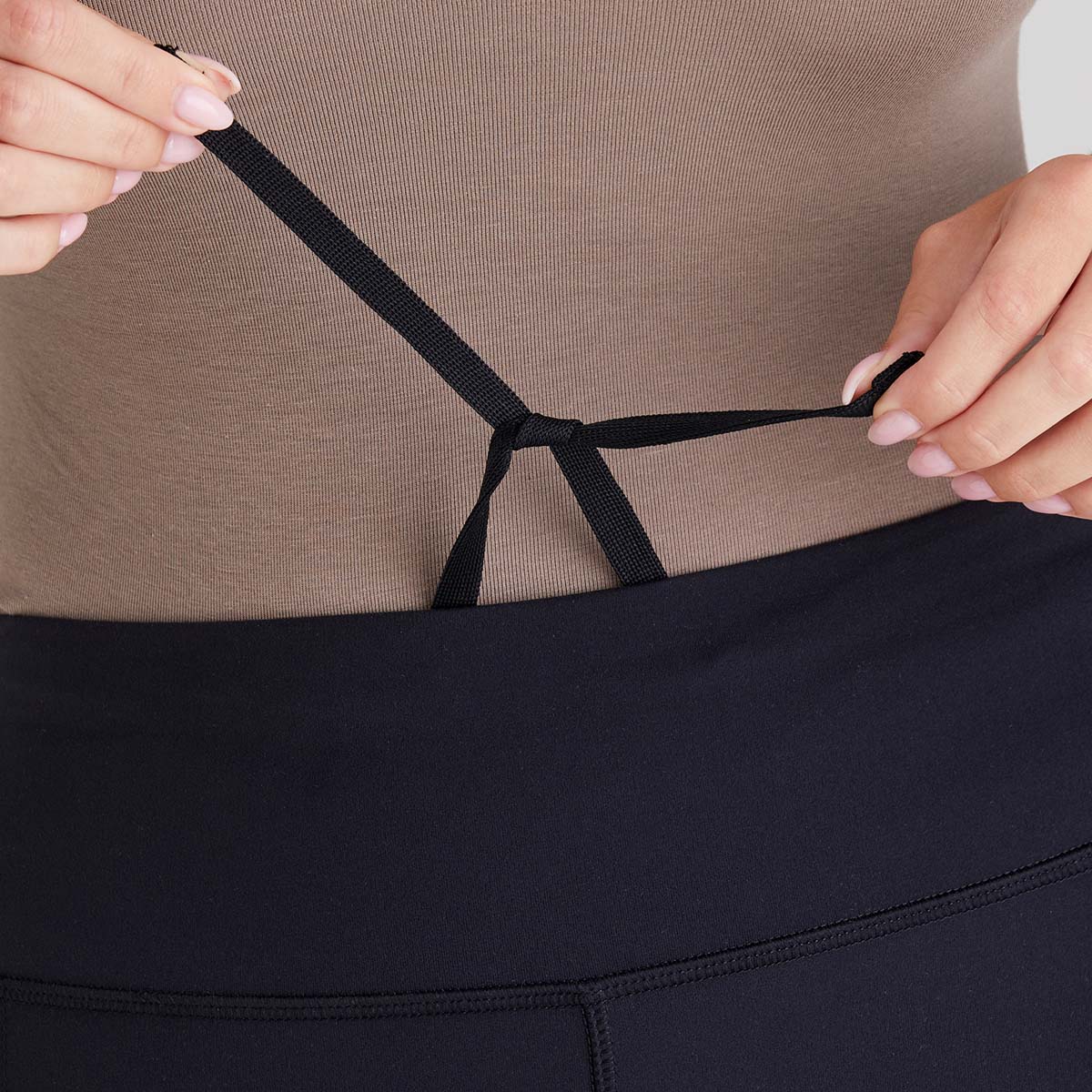 Person adjusting a waist drawstring with a neutral background