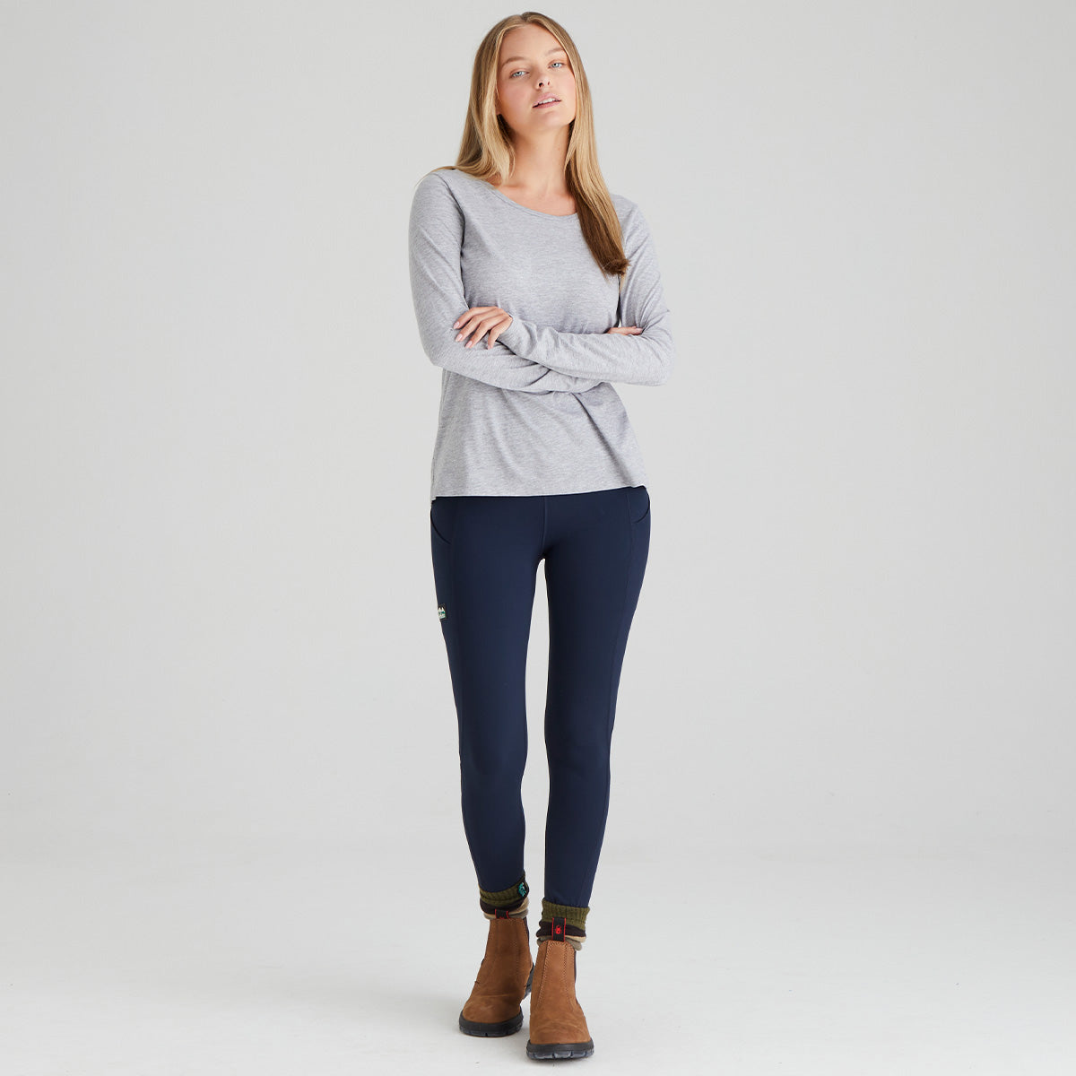 Woman wearing a gray long-sleeve top and navy leggings on a white background