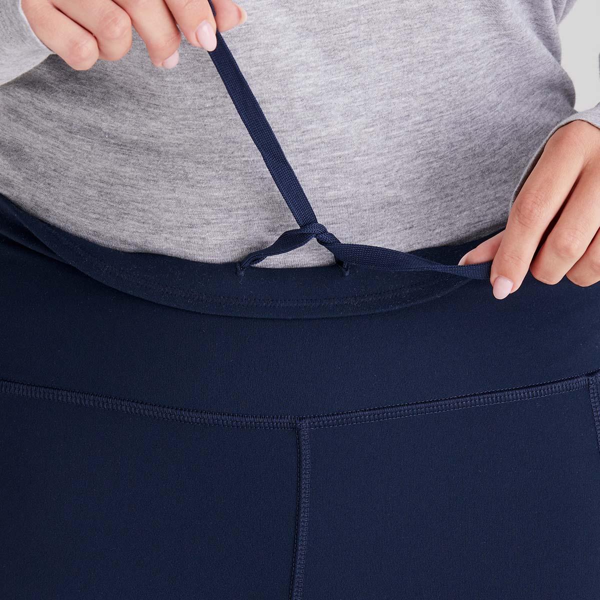 Person adjusting a navy drawstring on dark blue leggings with a grey top.