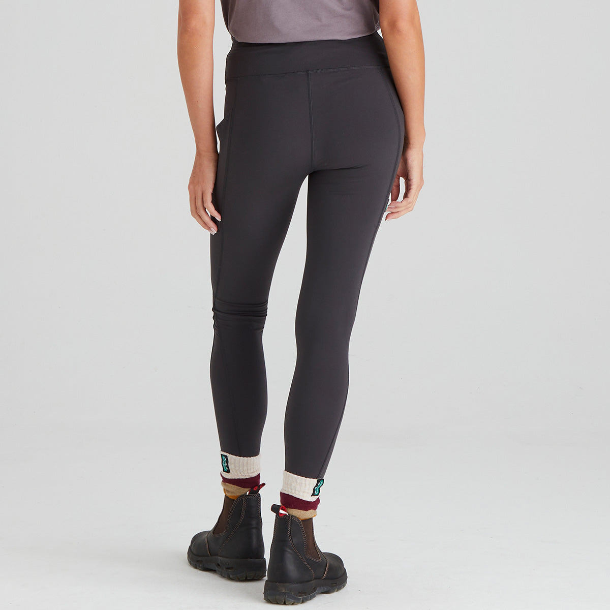 back view of a person wearing dark grey leggings with a plain background