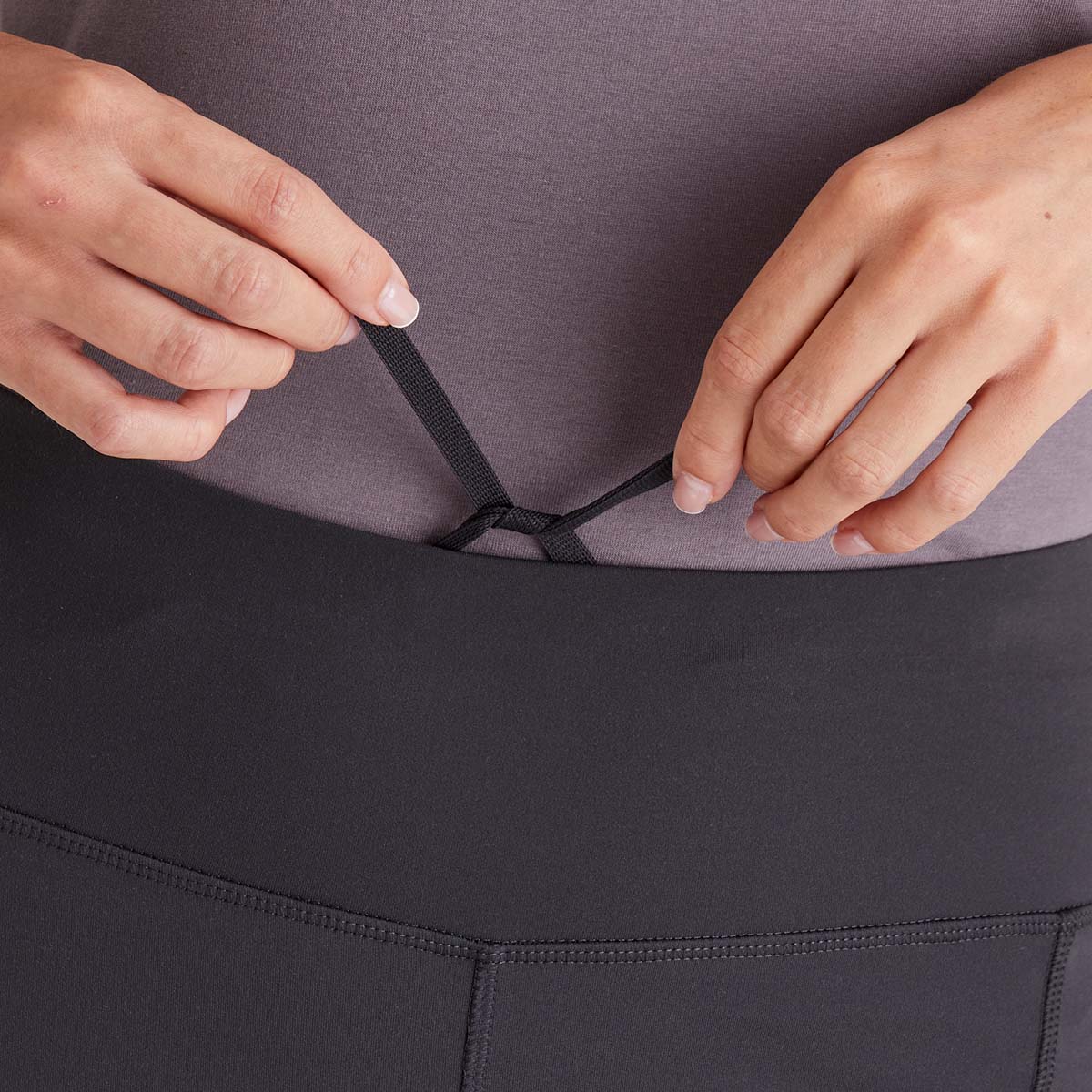 Person adjusting a black waistband on dark grey leggings.