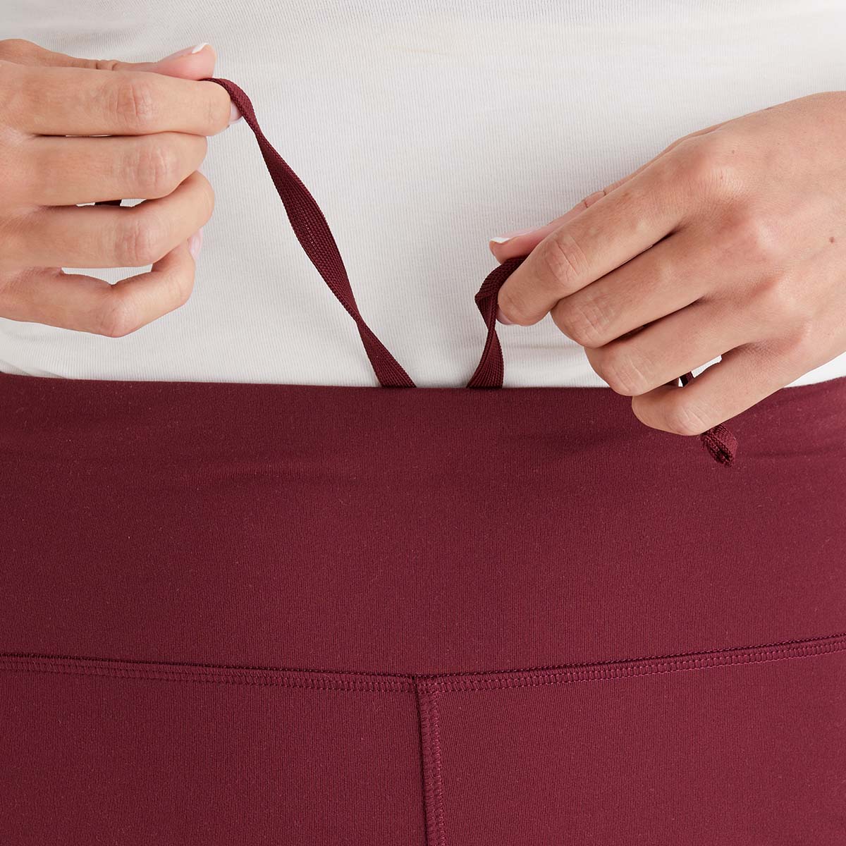 Close-up of a person adjusting the waistband of maroon leggings against a white background