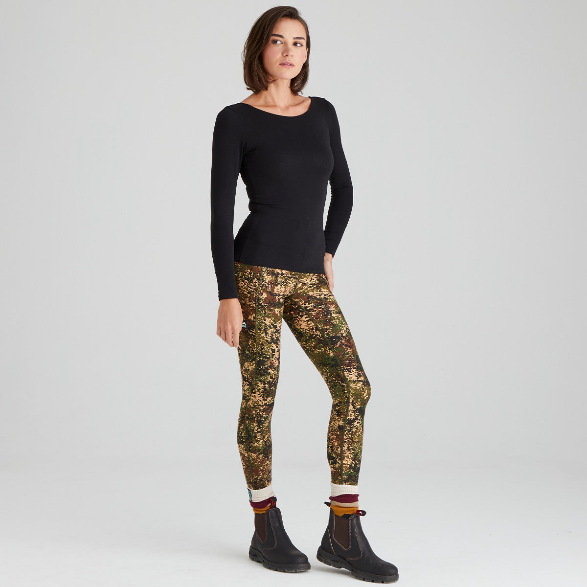 Woman wearing a black long-sleeve top and camouflage pants on a white background