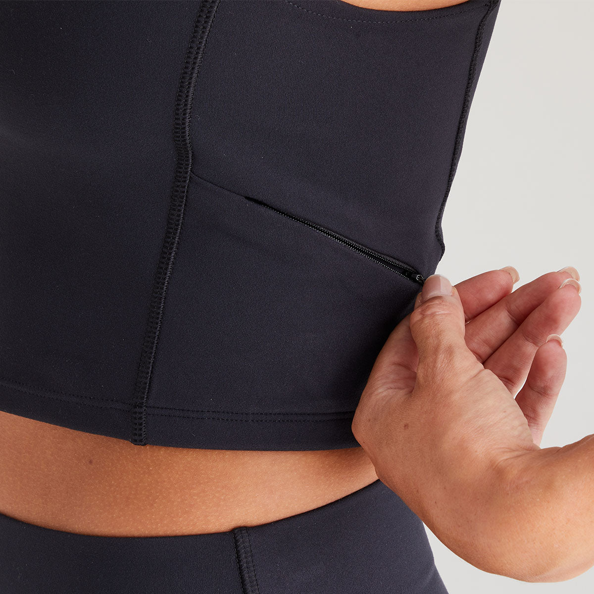 Person adjusting a black athletic top with a zipper on a neutral background