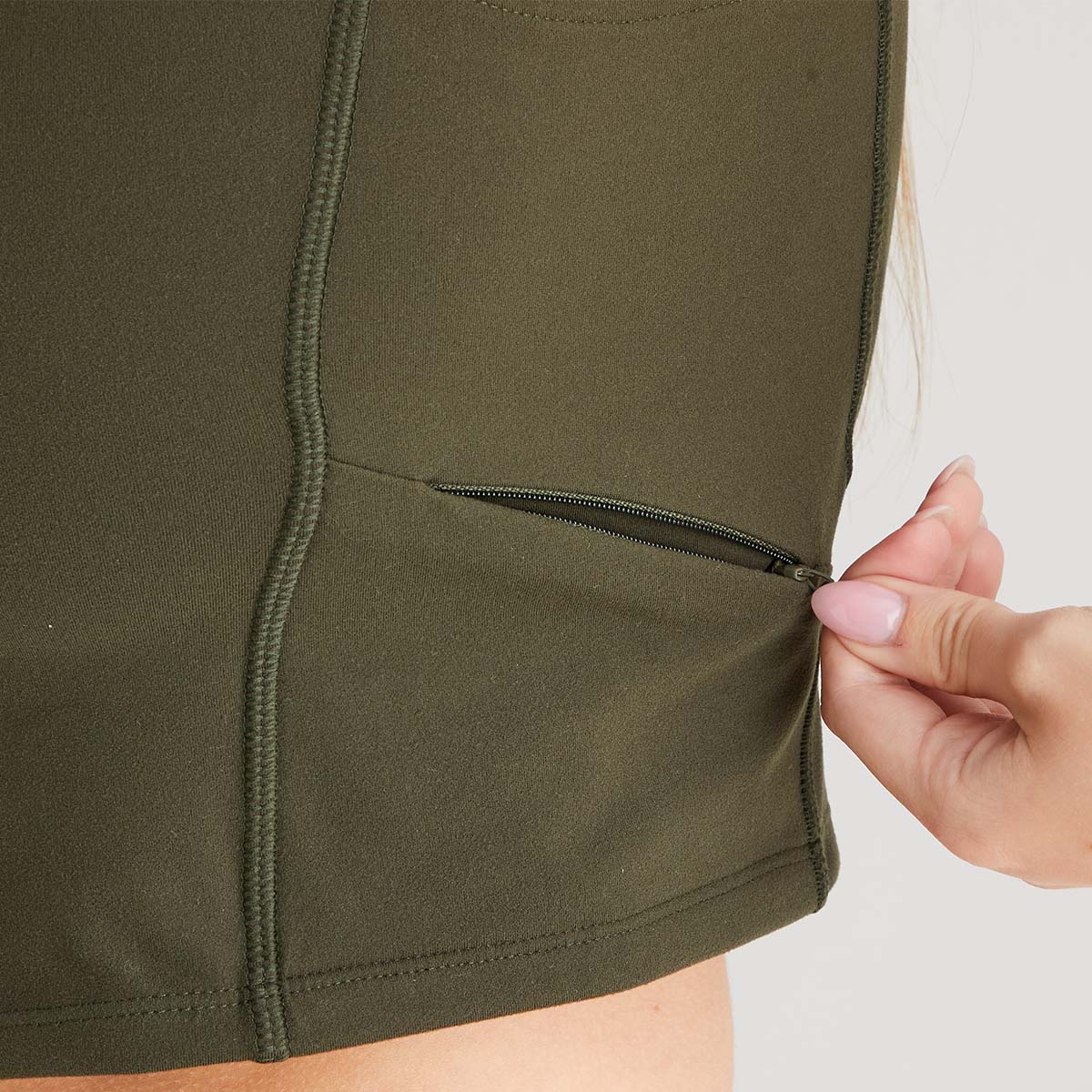 Close-up of a hand zipping up a green sleeveless top against a neutral background