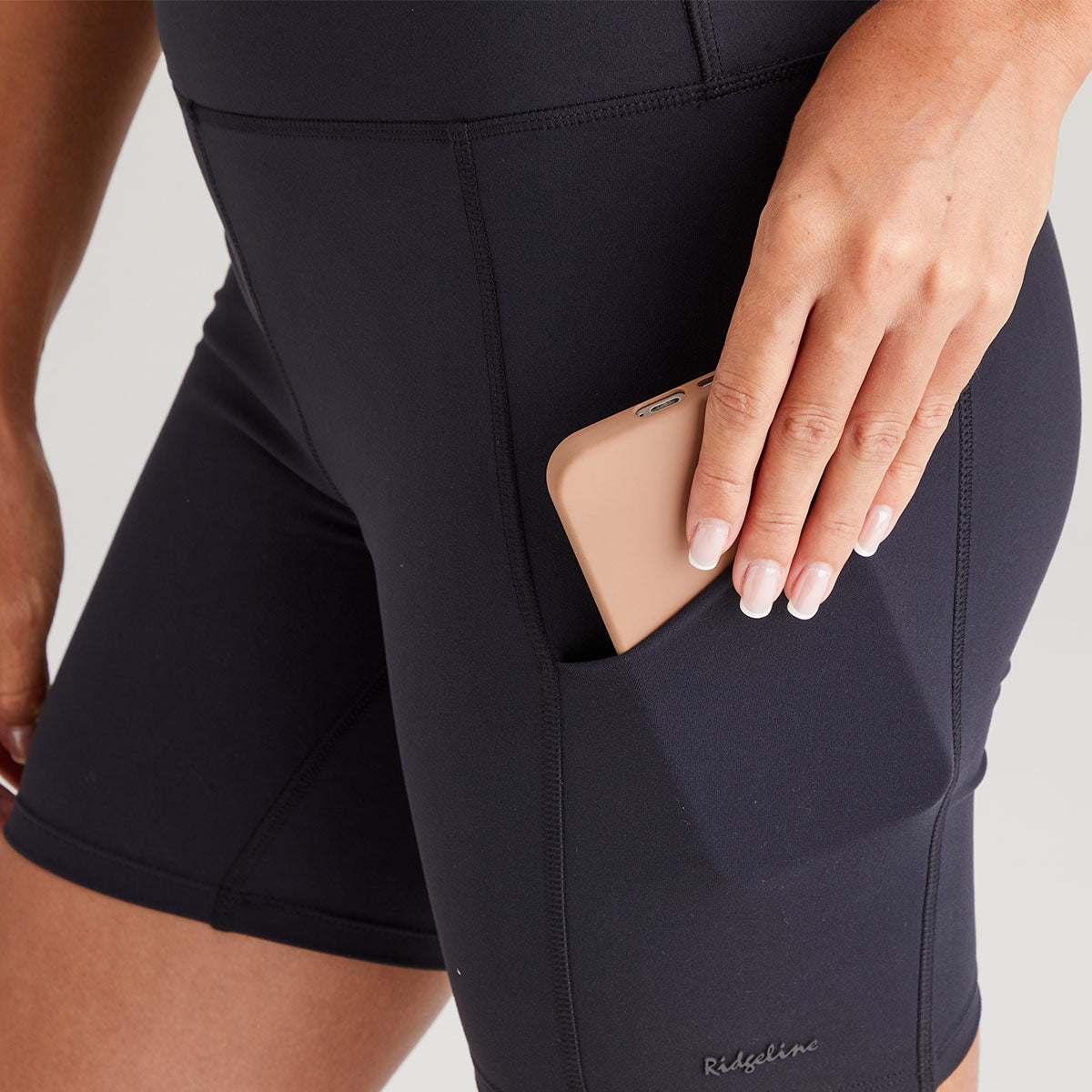 Person wearing black athletic shorts with a pocket, holding a beige phone case.