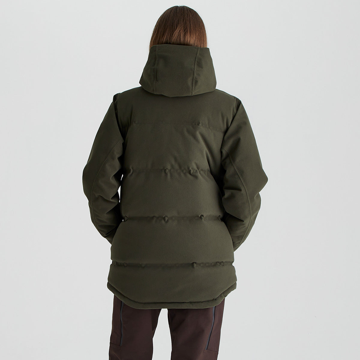 Rear view of a person wearing a Ridgeline olive green insulated hooded jacket with a padded design and extended back hem, paired with dark trousers, shown against a light grey studio background.