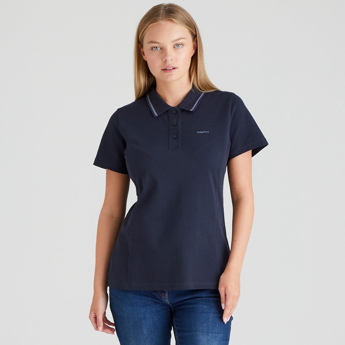 Woman wearing a navy polo shirt with a ridgeline clothing brand logo on a grey background