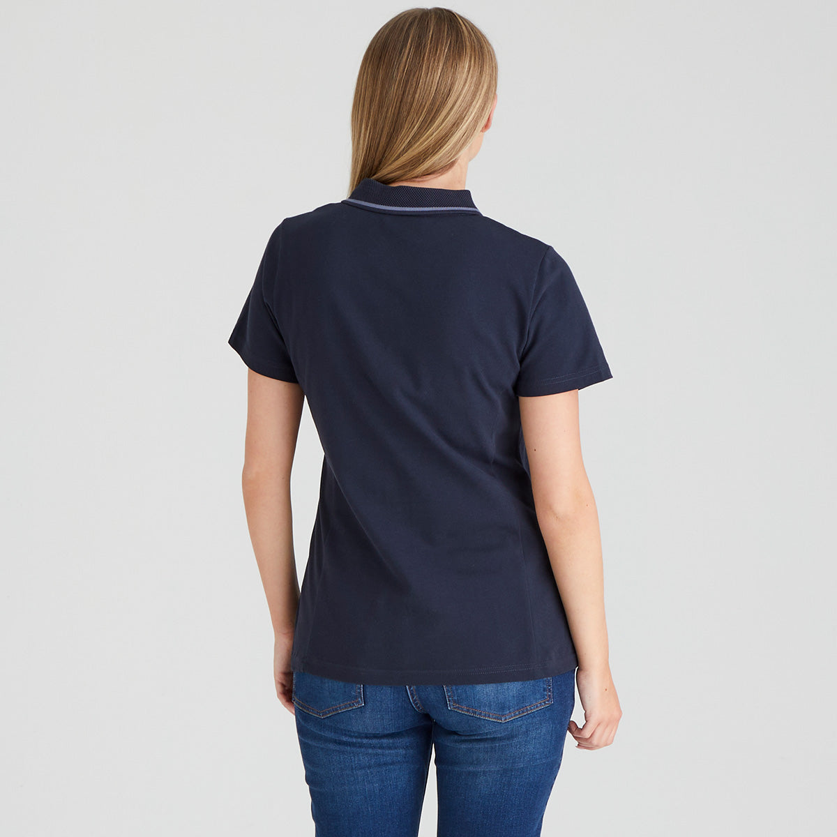 Person wearing a navy blue polo shirt and blue jeans on a light gray background