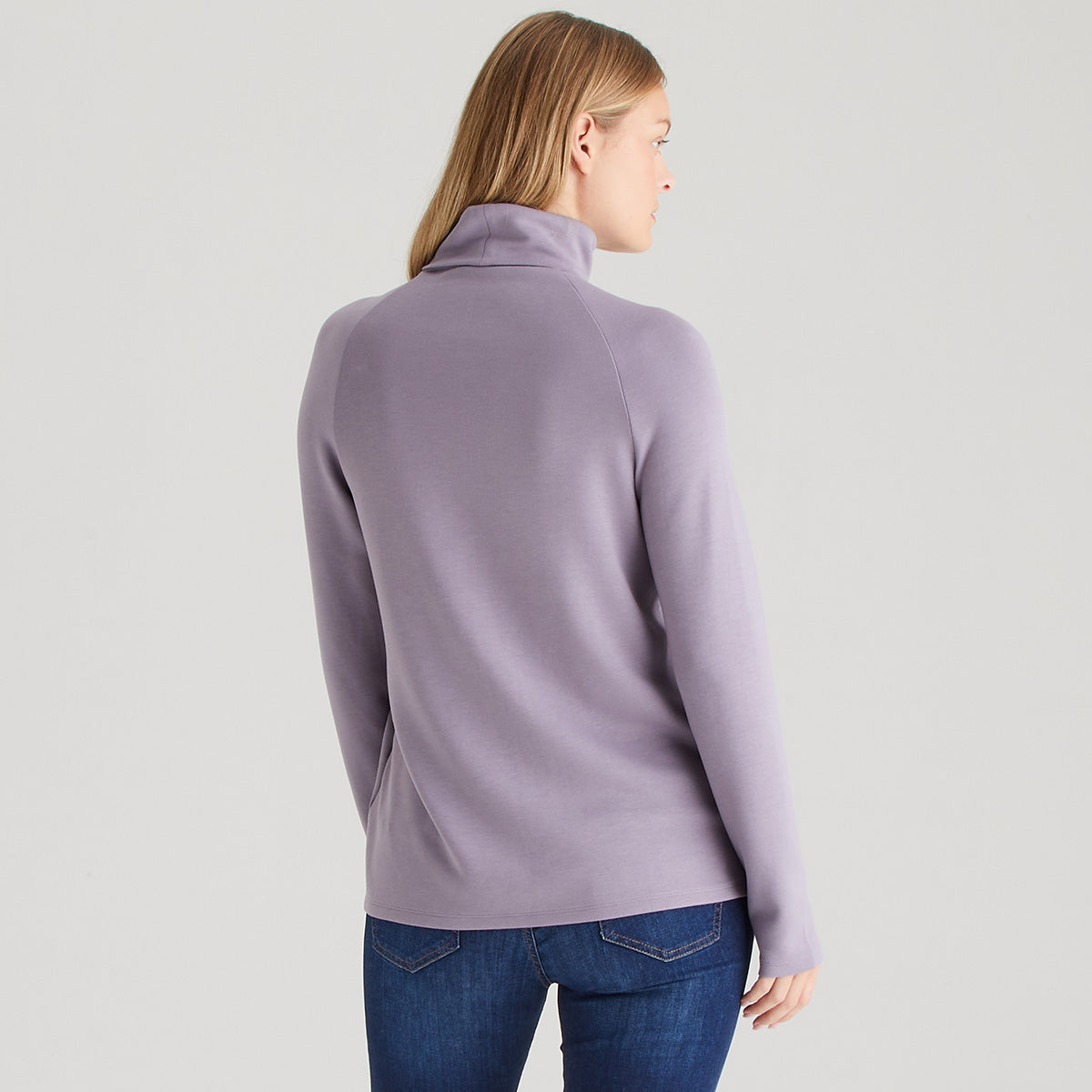 Person wearing a light purple sweater and blue jeans on a plain background