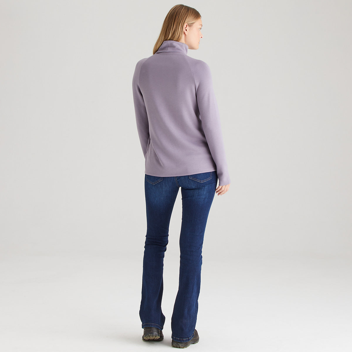 Person wearing a light purple turtleneck and blue jeans on a white background
