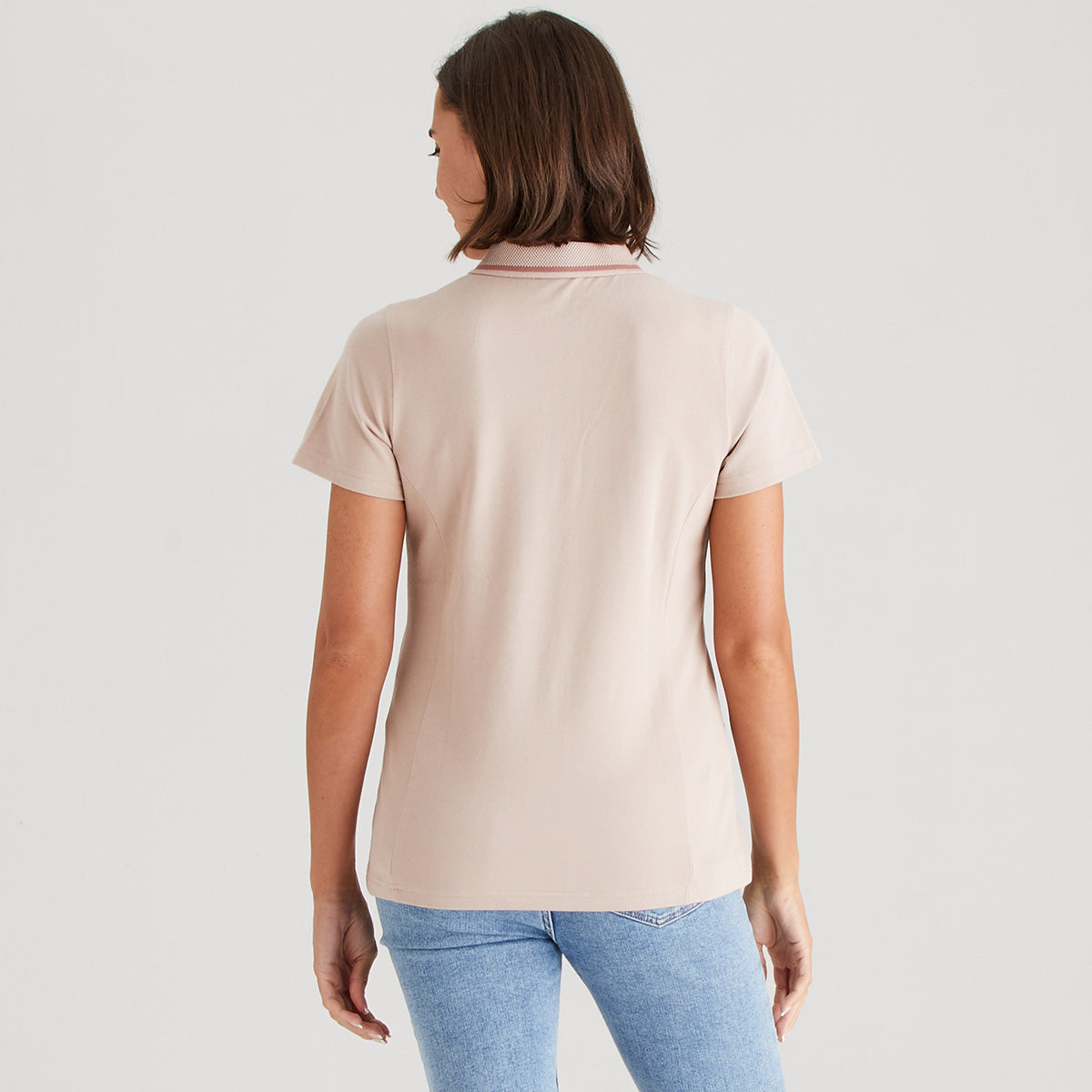 Woman wearing a blush polo shirt and blue jeans on a light gray background