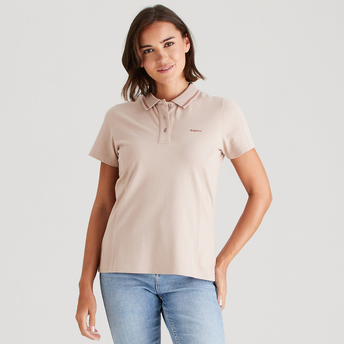 Woman wearing a pink polo shirt and blue jeans on a plain background