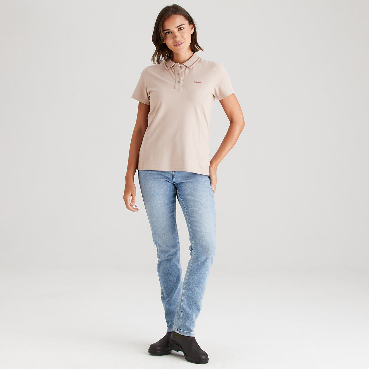 Woman wearing a beige polo shirt and light blue jeans on a white background