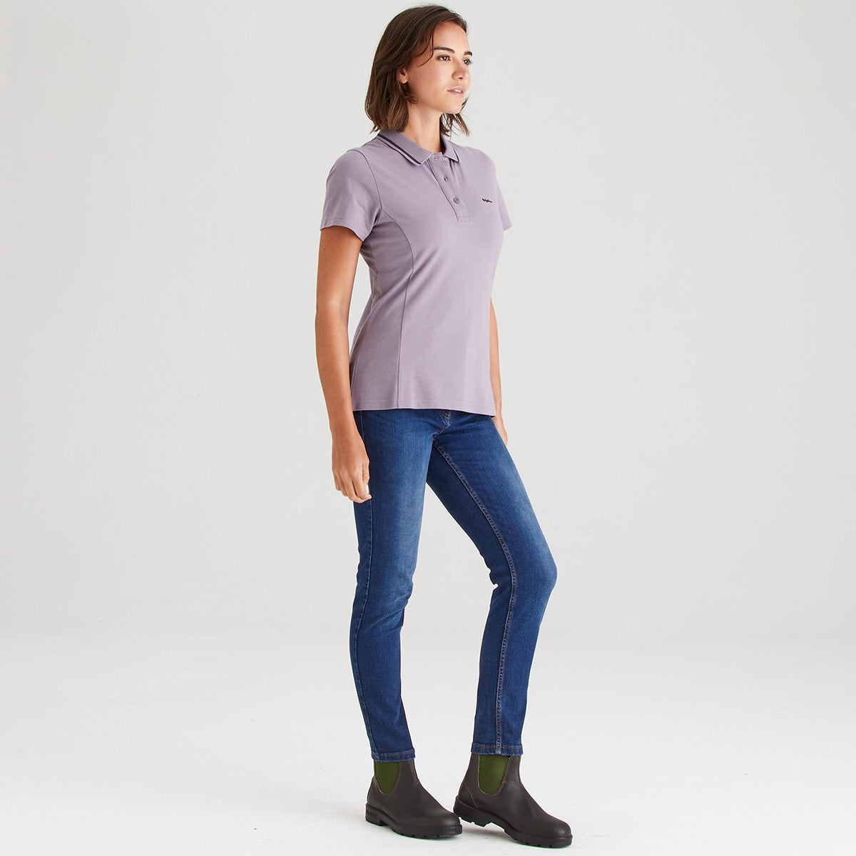 Woman wearing a purple polo shirt and blue jeans on a white background