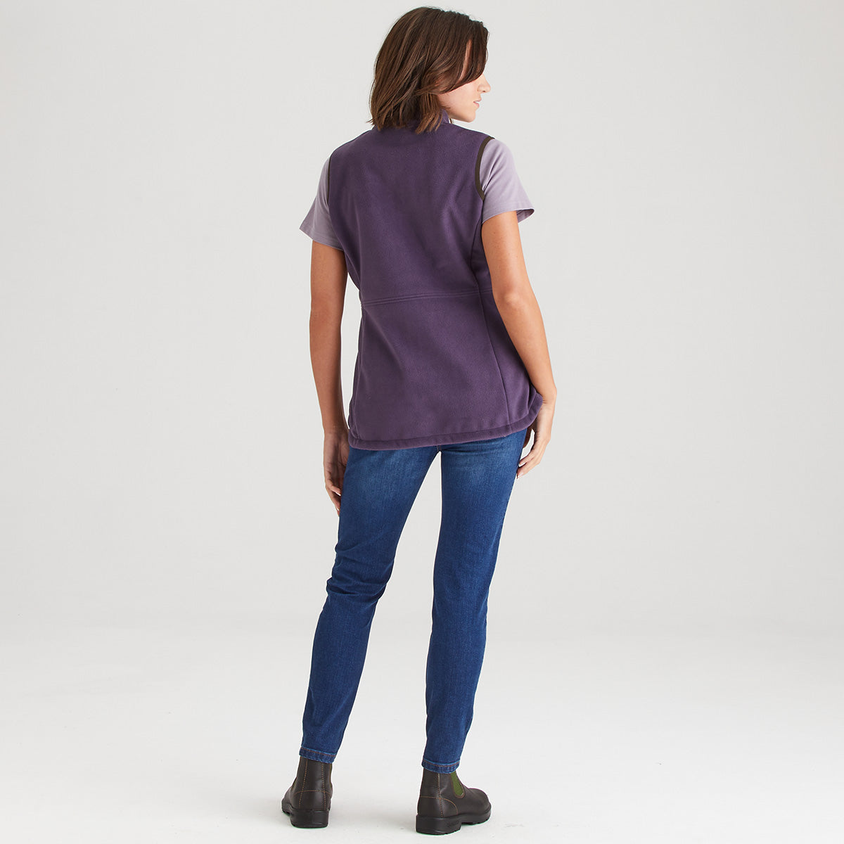 Person wearing a purple vest over a t-shirt with blue jeans on a white background