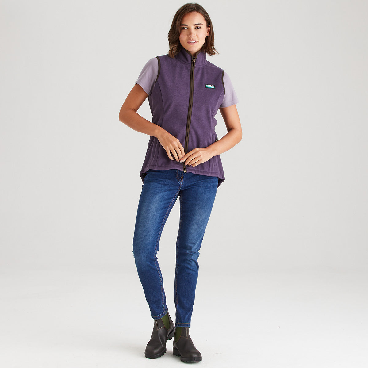 Woman wearing a purple vest and blue jeans on a white background