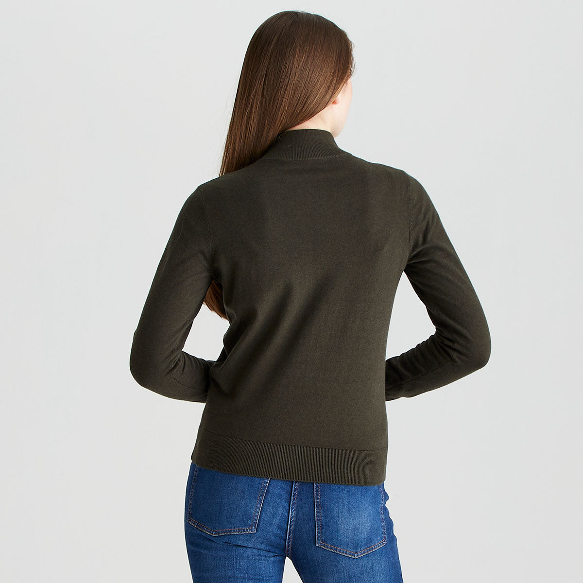 Rear view of a person wearing a dark olive-green long-sleeve quarter-zip knit sweater and blue jeans, standing against a plain light gray studio background. The sweater features a high collar, fitted silhouette, and ribbed hem. Long hair falls down the back, partially covering the upper section of the sweater. The image highlights the back fit, fabric texture, and overall garment design.