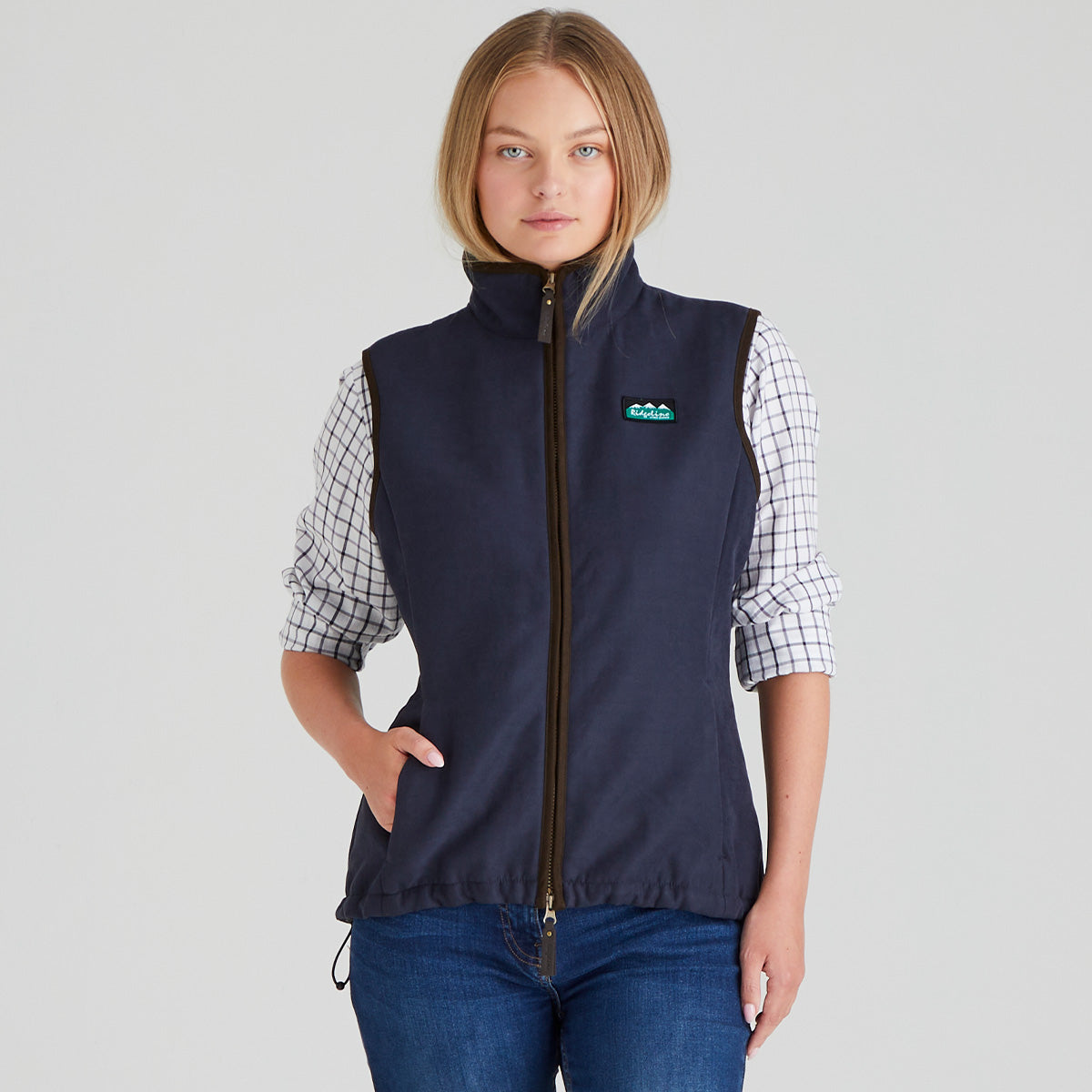 Woman wearing a navy blue moleskin gilet vest with a ridgeline clothing brand logo on a grey background