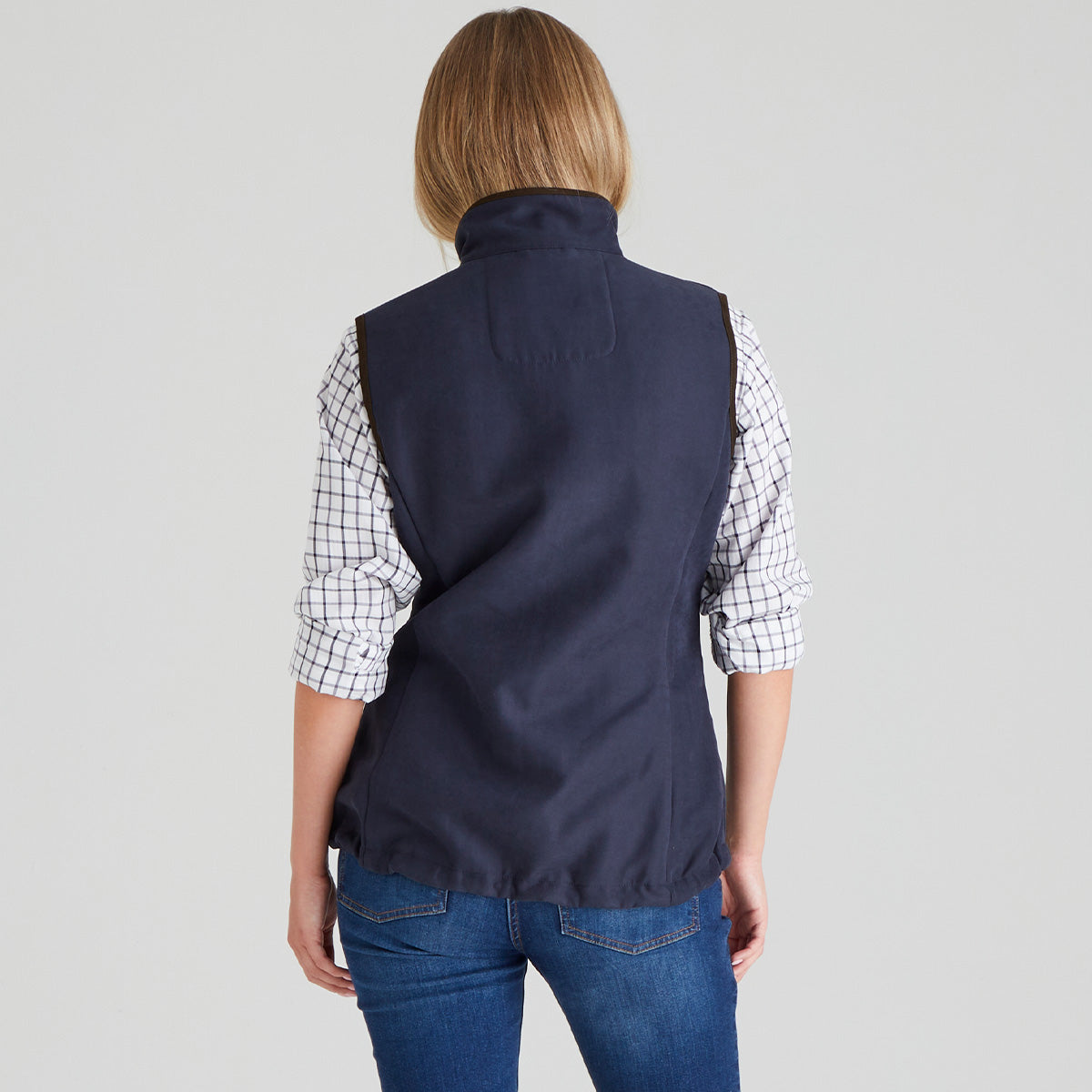 Person wearing a navy gilet vest over a plaid shirt on a grey background