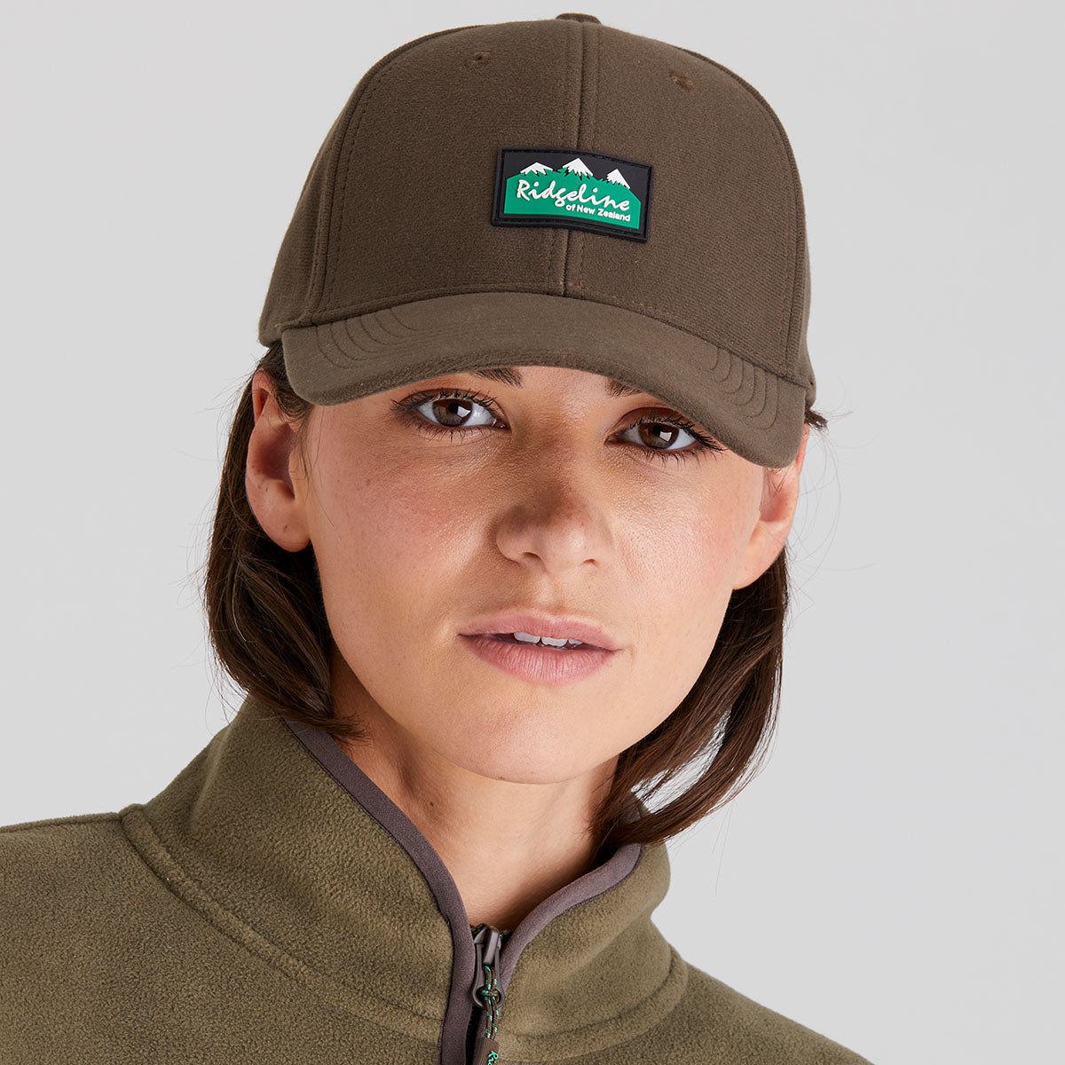 Person wearing a brown cap with a logo and matching jacket on a gray background