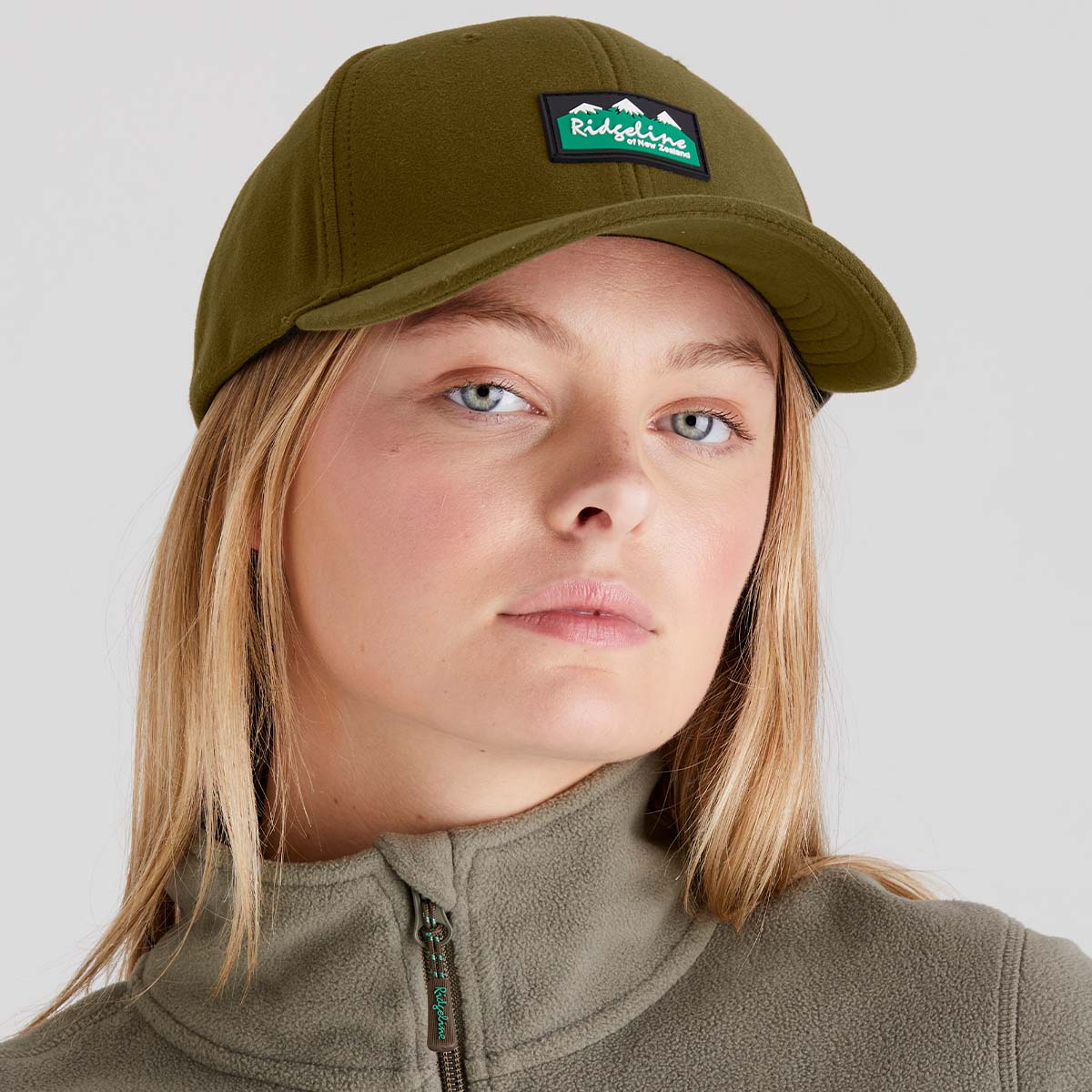 Person wearing a brown cap with a logo and matching jacket on a light grey background
