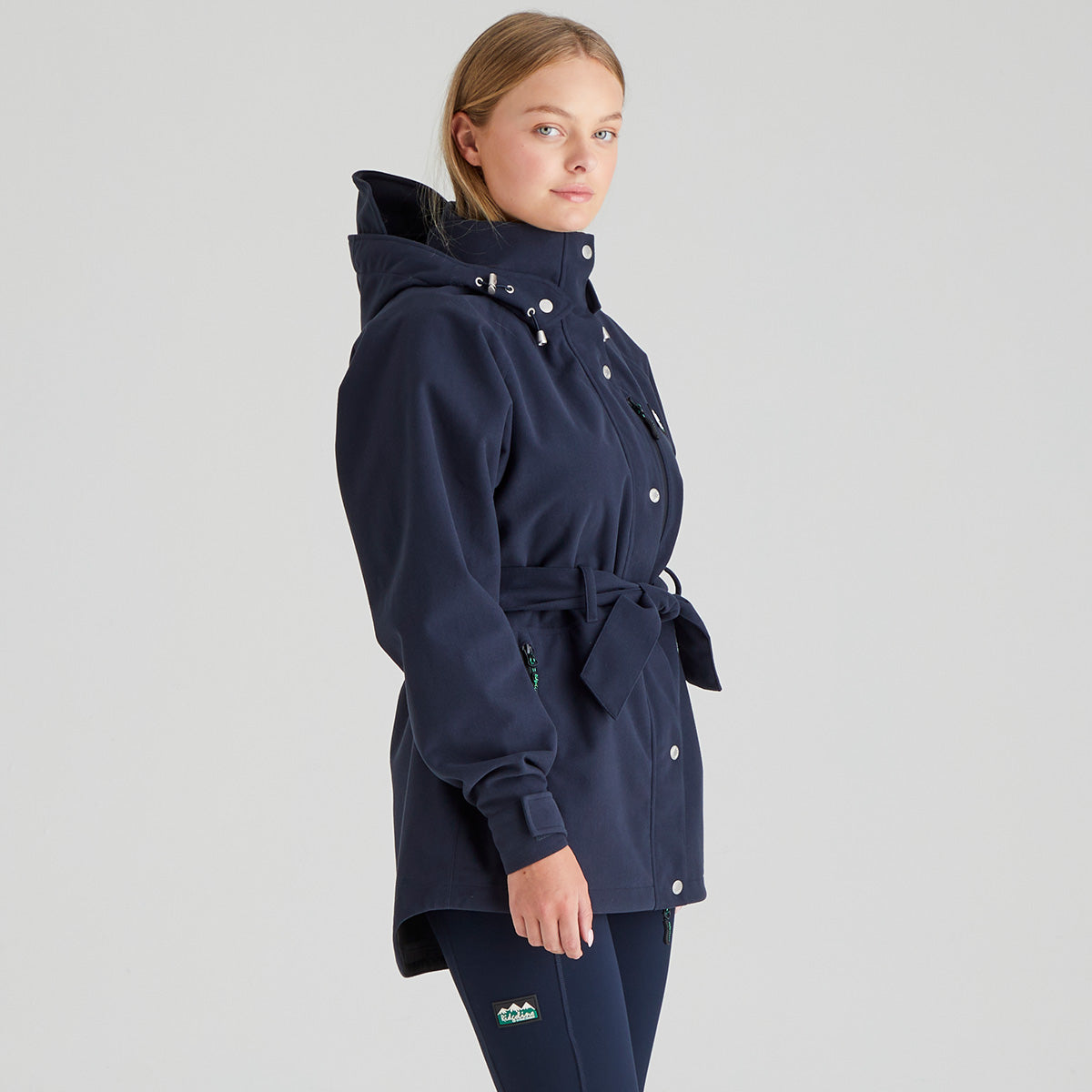 Woman wearing a navy blue coat with a belt on a light gray background