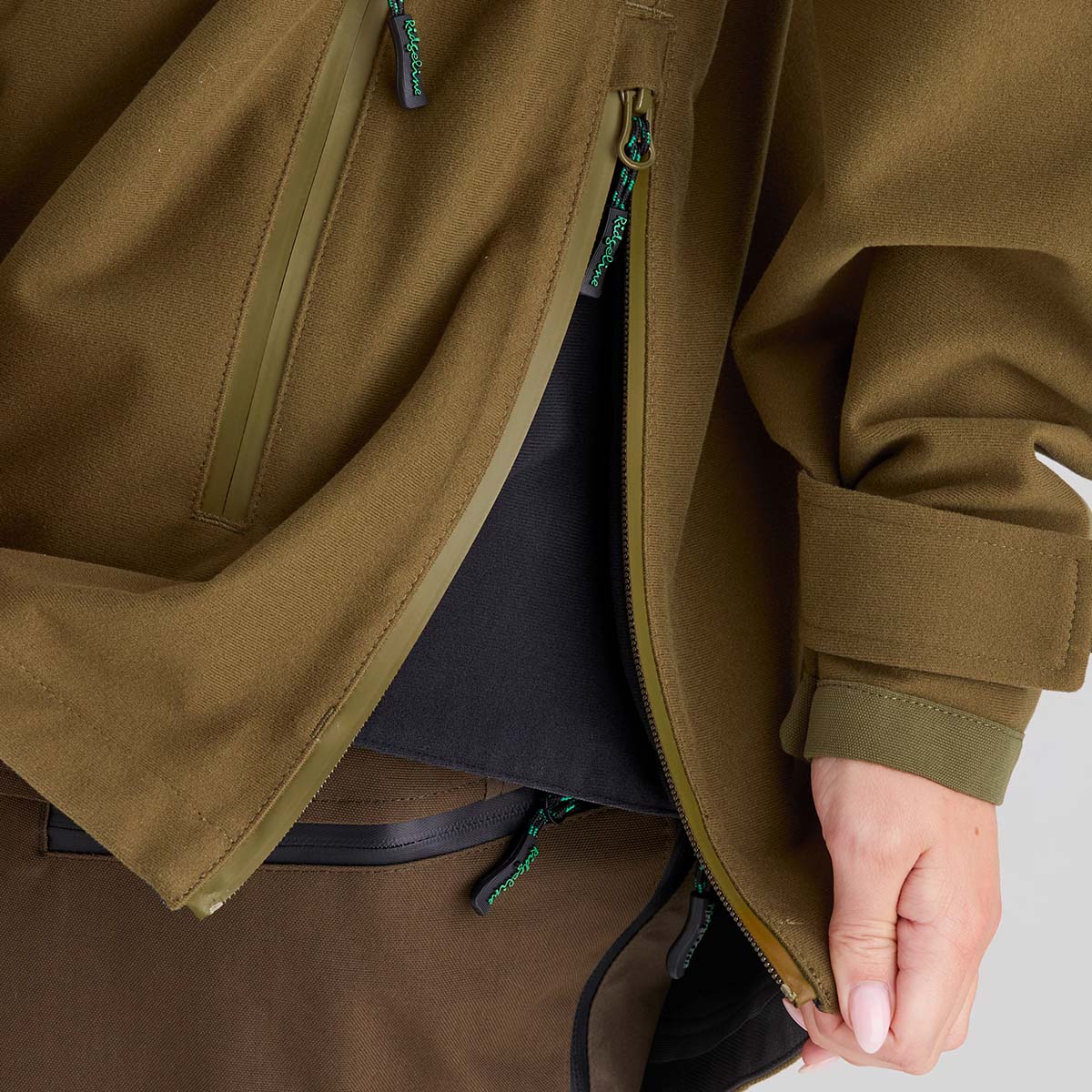 Close-up of a brown jacket with a hand opening the side zipper.
