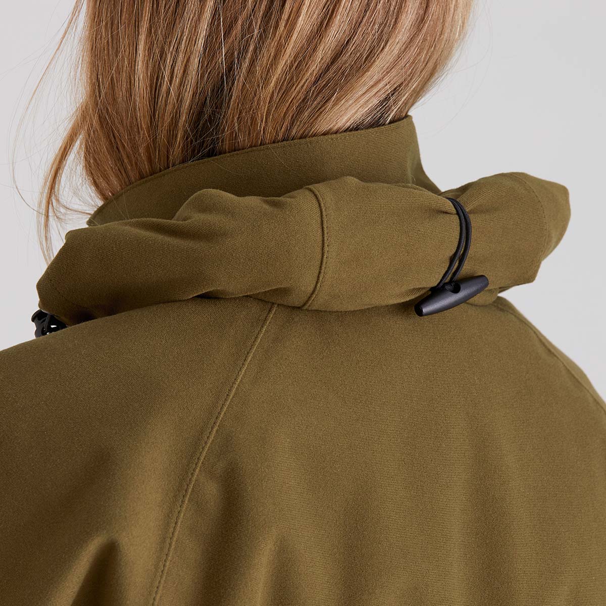 Close-up of a person wearing a brown coat with the hood rolled up on a white background
