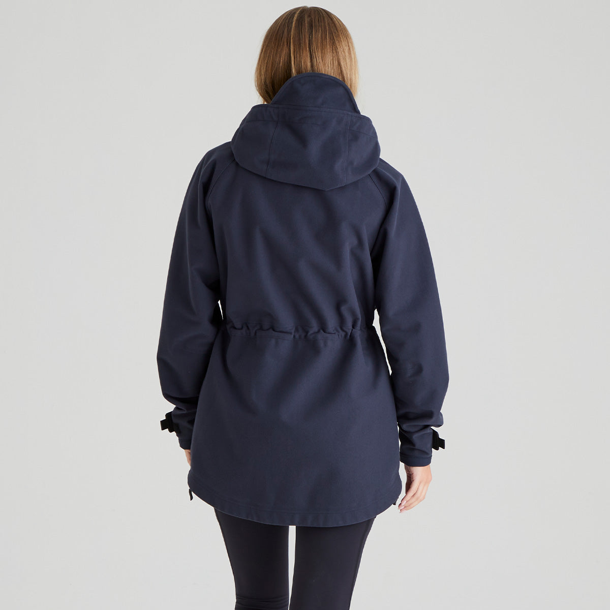 back view of woman wearing a navy blue hooded coat on a light grey background