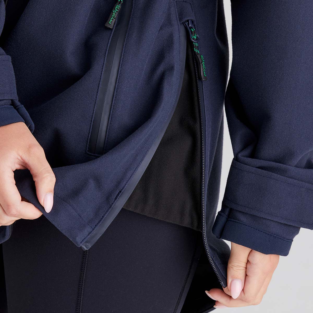 Person wearing a navy blue jacket with a close-up of the zipper for side vent