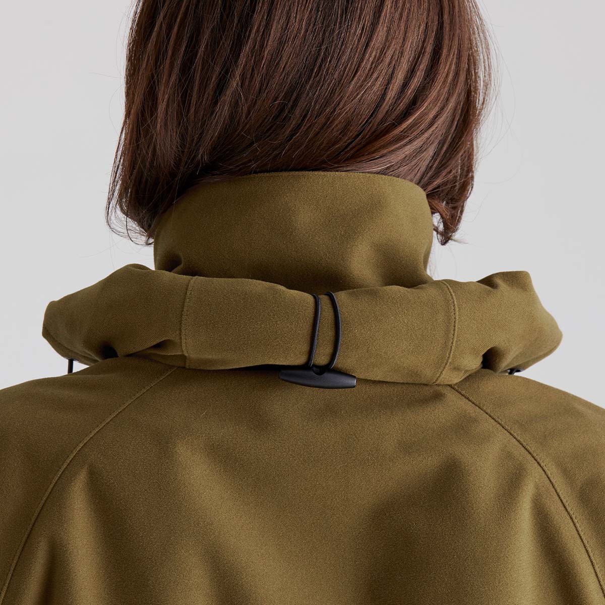 Close-up of a person wearing a brown coat rolled up hood with a plain background